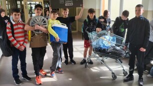Grupa chłopców pokazuje swoje plecaki- m.in. wózek sklepowy, felgę, lodówkę przenośną